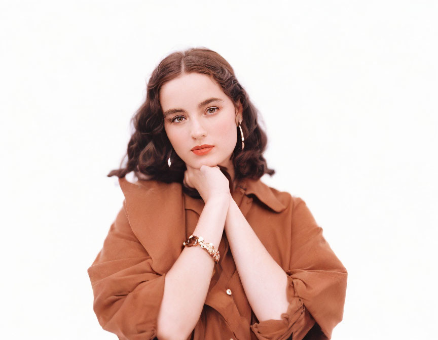 Curly-haired woman in brown blouse with gold accessories on white background