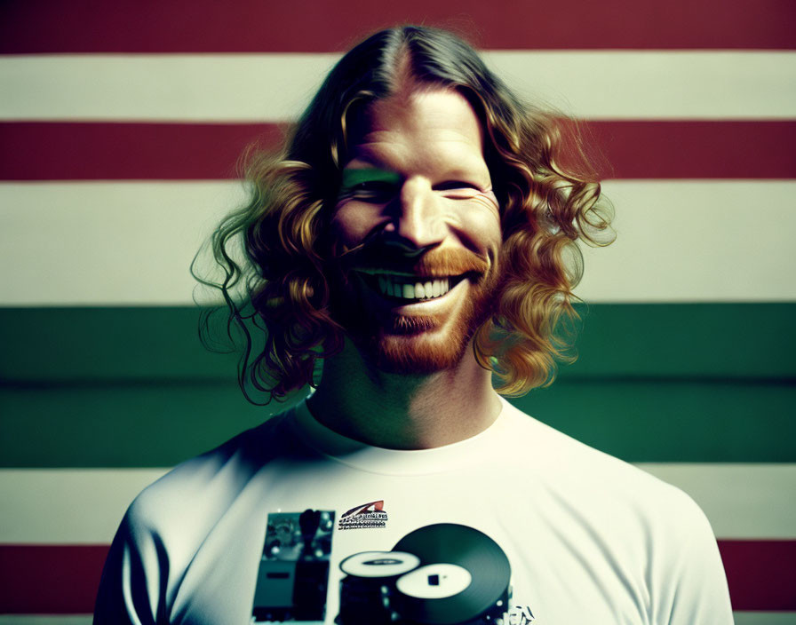 Smiling man with curly hair and beard in white T-shirt on striped background