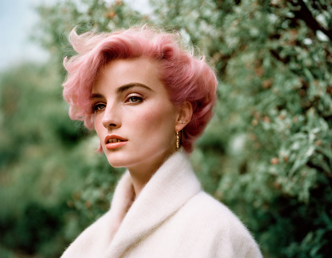 Pink-haired woman in vintage style posing elegantly in white coat amid lush greenery