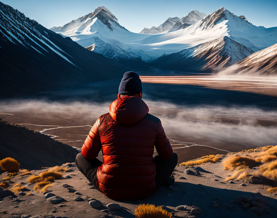 Person in red jacket admiring majestic mountain range at sunrise