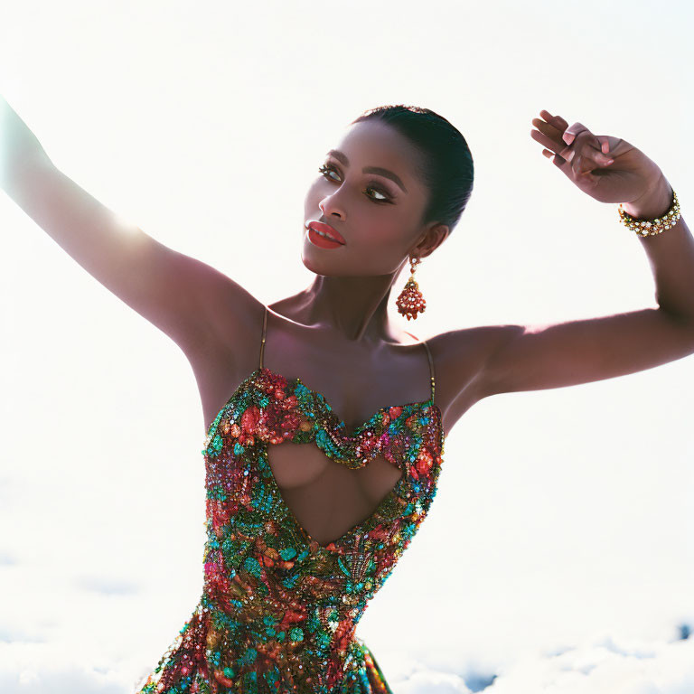 Elegant woman in multicolored dress and jewelry poses gracefully against bright sky.