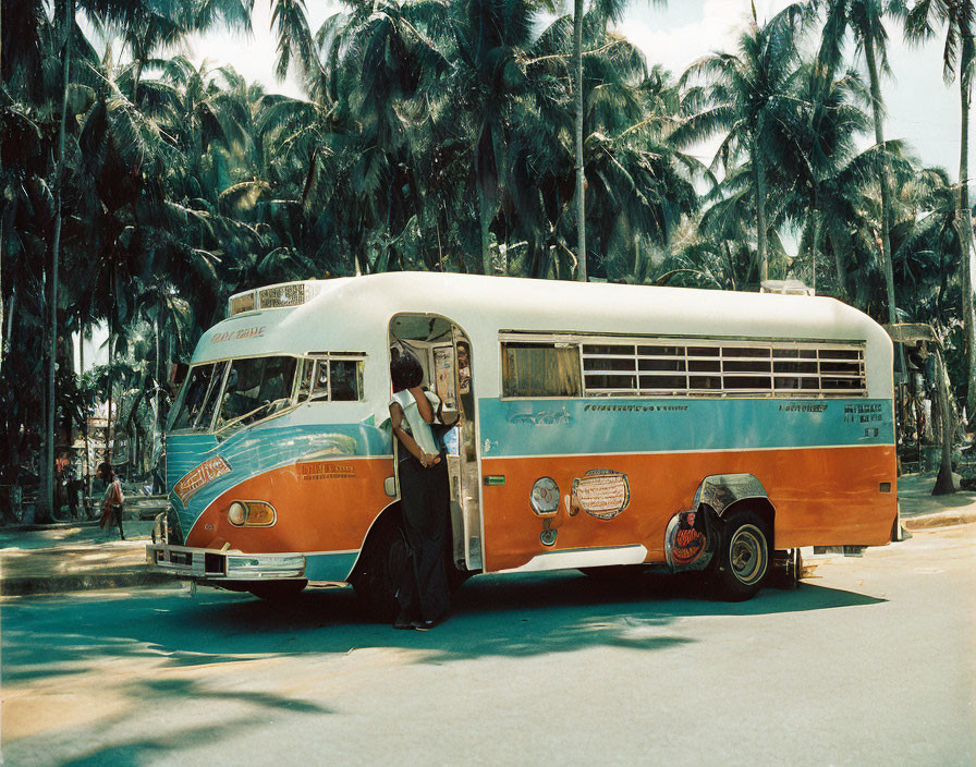 Vintage Orange and White Bus with Driver Parked Under Palm Trees