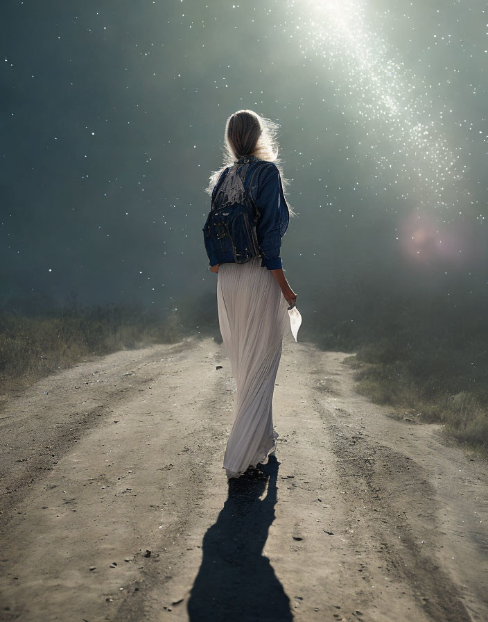 Person in denim jacket and white skirt walking on dusty path under sunbeams