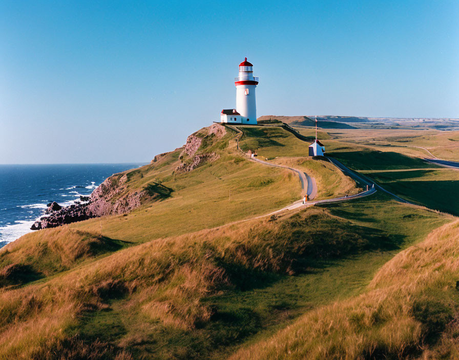 White Lighthouse with Red Top on Grassy Cliff by Calm Blue Sea