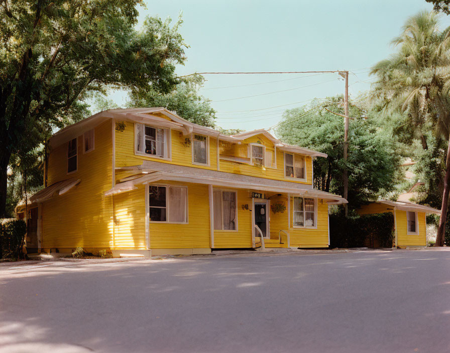 Yellow Two-Story Building with White Trim and Porch Surrounded by Trees