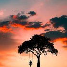 Solitary tree on hill with swing under orange sky, moon, and planet