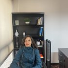 Woman in Blue Coat Sitting at Desk with Bookshelf and Decorative Items