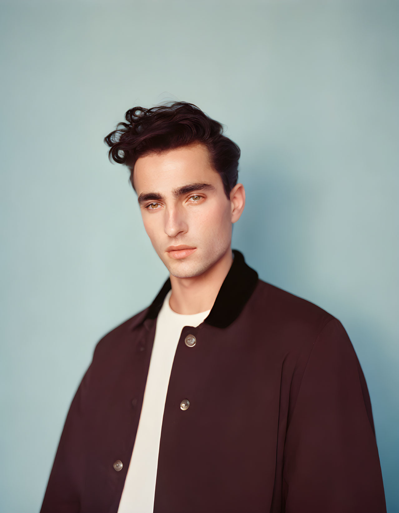 Young man with dark hair in dark jacket against pale blue background