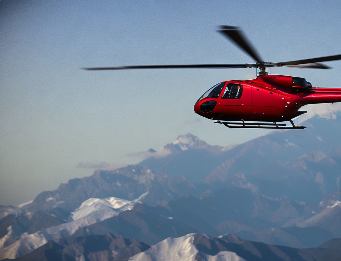 Red Helicopter Flying Over Mountain Range in Clear Blue Sky