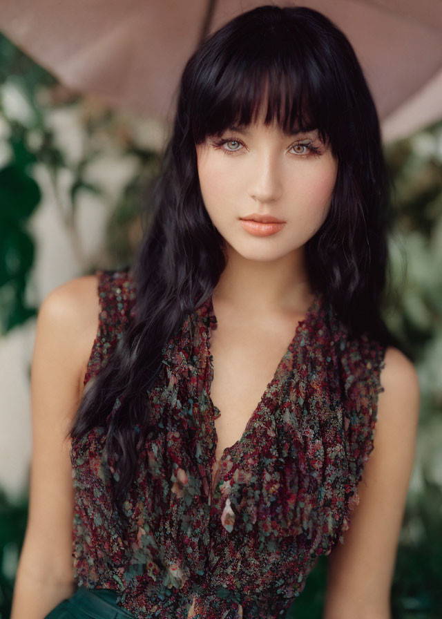 Woman with dark hair and floral top holding umbrella, gazing ahead.