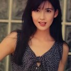 Woman with dark hair and floral top holding umbrella, gazing ahead.