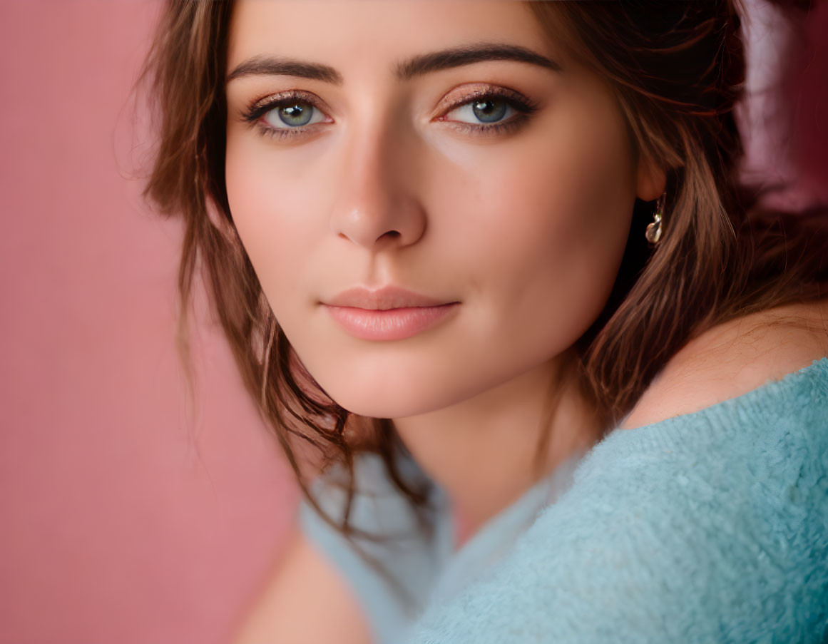 Portrait of woman with brown hair and eyes in blue top on pink background