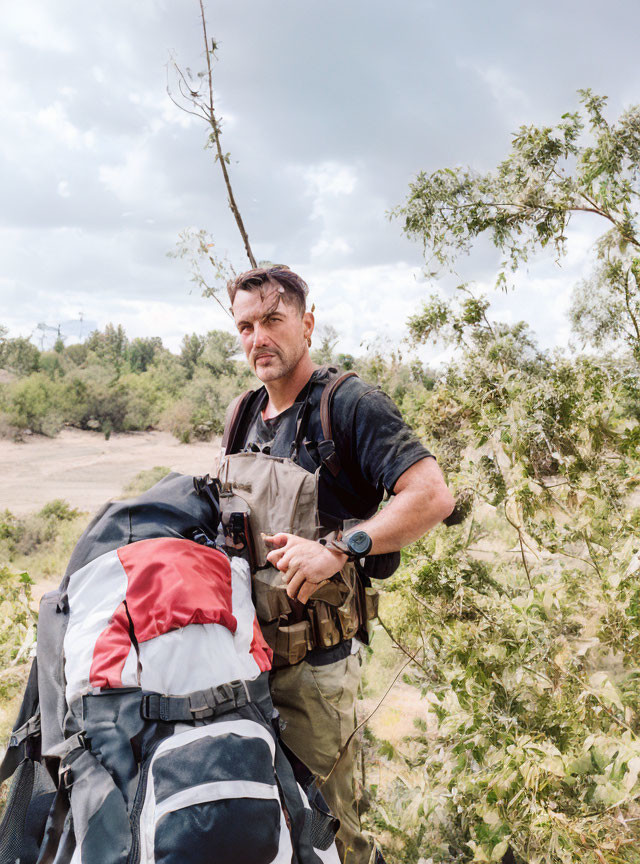 Man with backpack and binoculars in bushy terrain showing attentiveness.