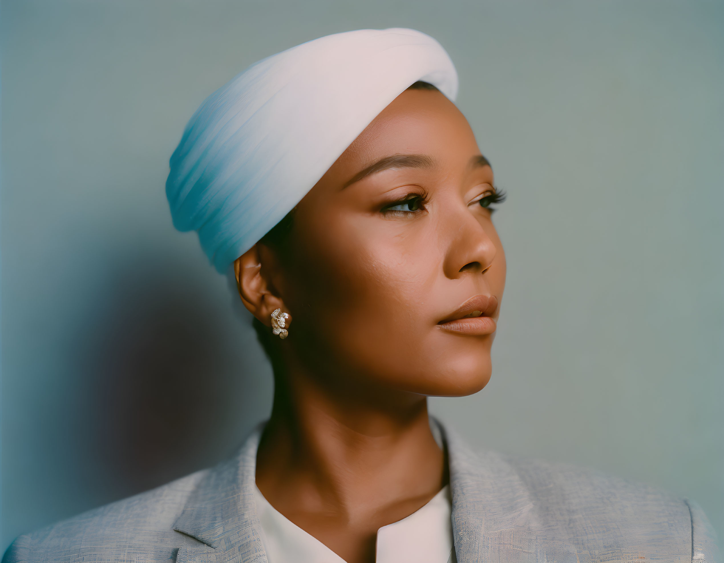 Serene person in white headwrap and gray blazer, looking sideways on aqua background