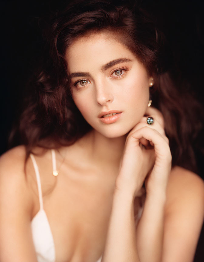 Portrait of Woman with Brown Hair and Striking Eyes in White Top on Dark Background