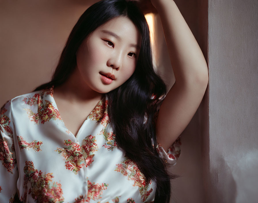 Woman in Floral Top Poses by Wall in Soft Lighting