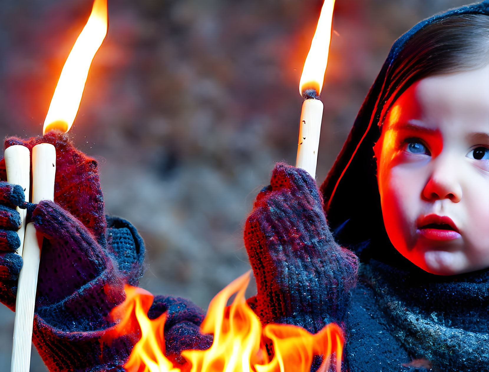 Child in Blue Hooded Garment Holding Flaming Torches