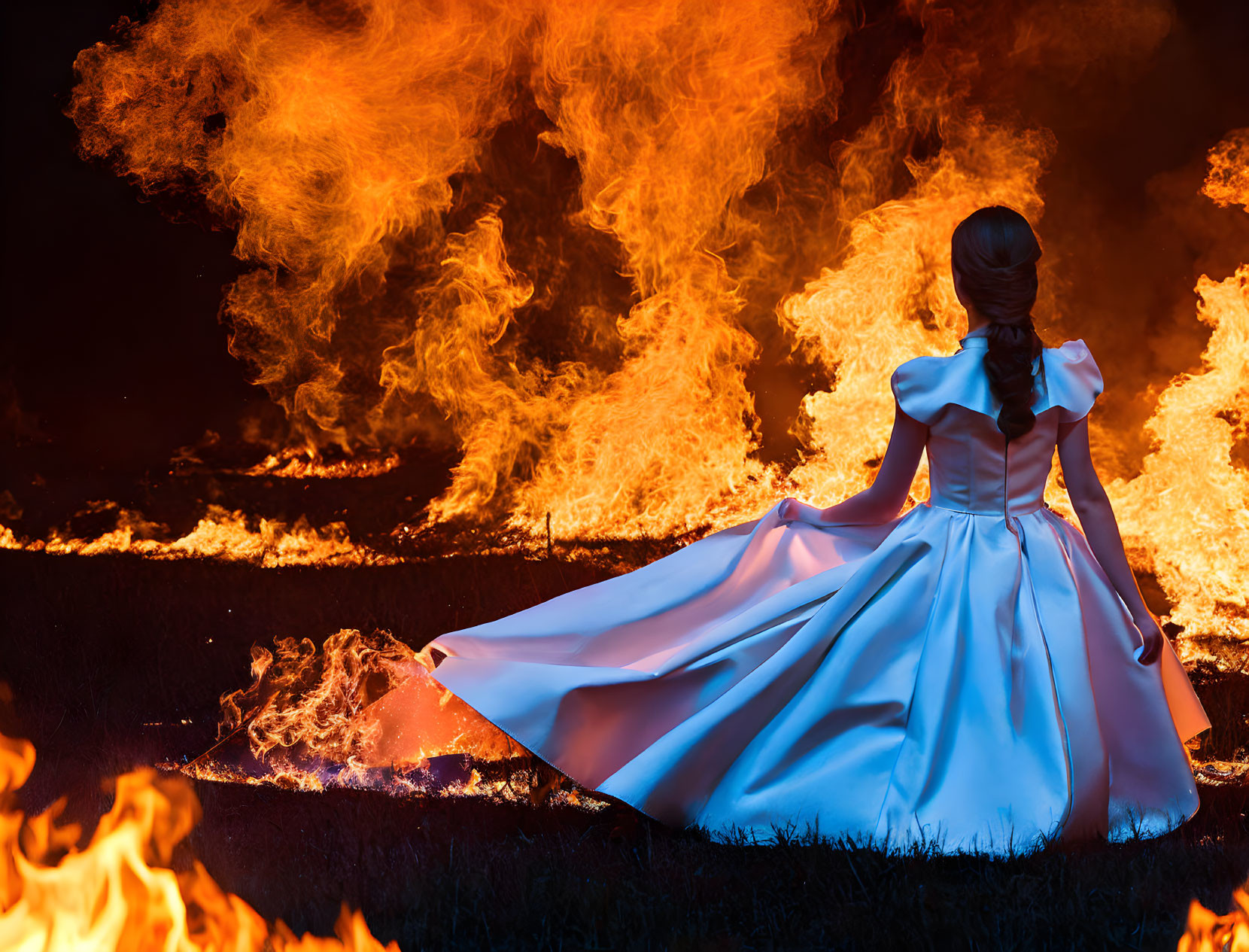 Woman in white dress sitting by fierce fire at night surrounded by darkness