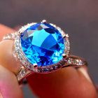 Close-up of hand holding blue gemstone ring with diamonds on silver band