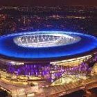 Modern illuminated stadium at night with blue glow amidst cityscape