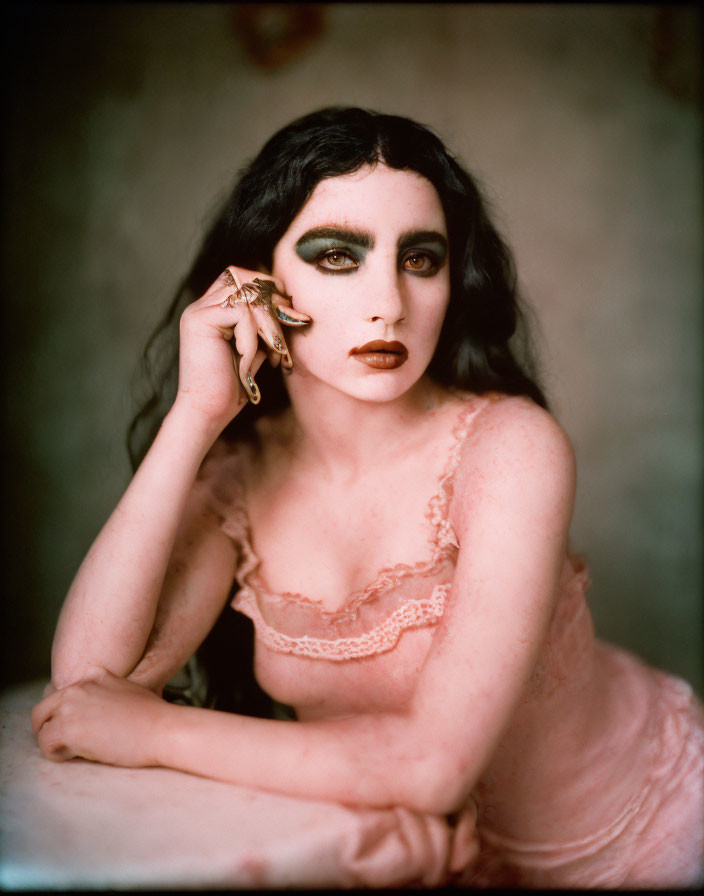 Person with dramatic makeup in pink lace top and ring, gazing at camera