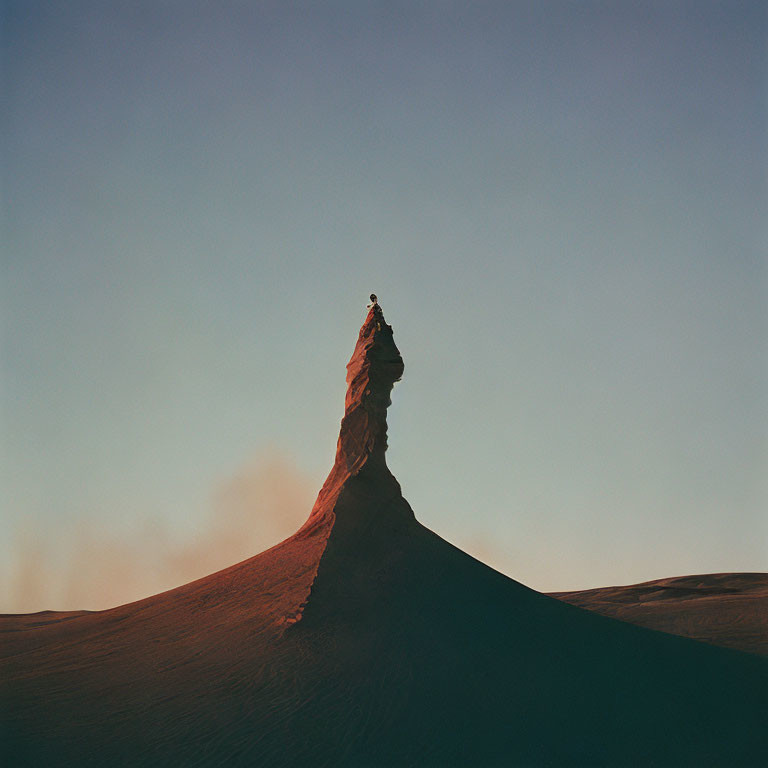 Person standing on tall sandstone formation in desert at dusk