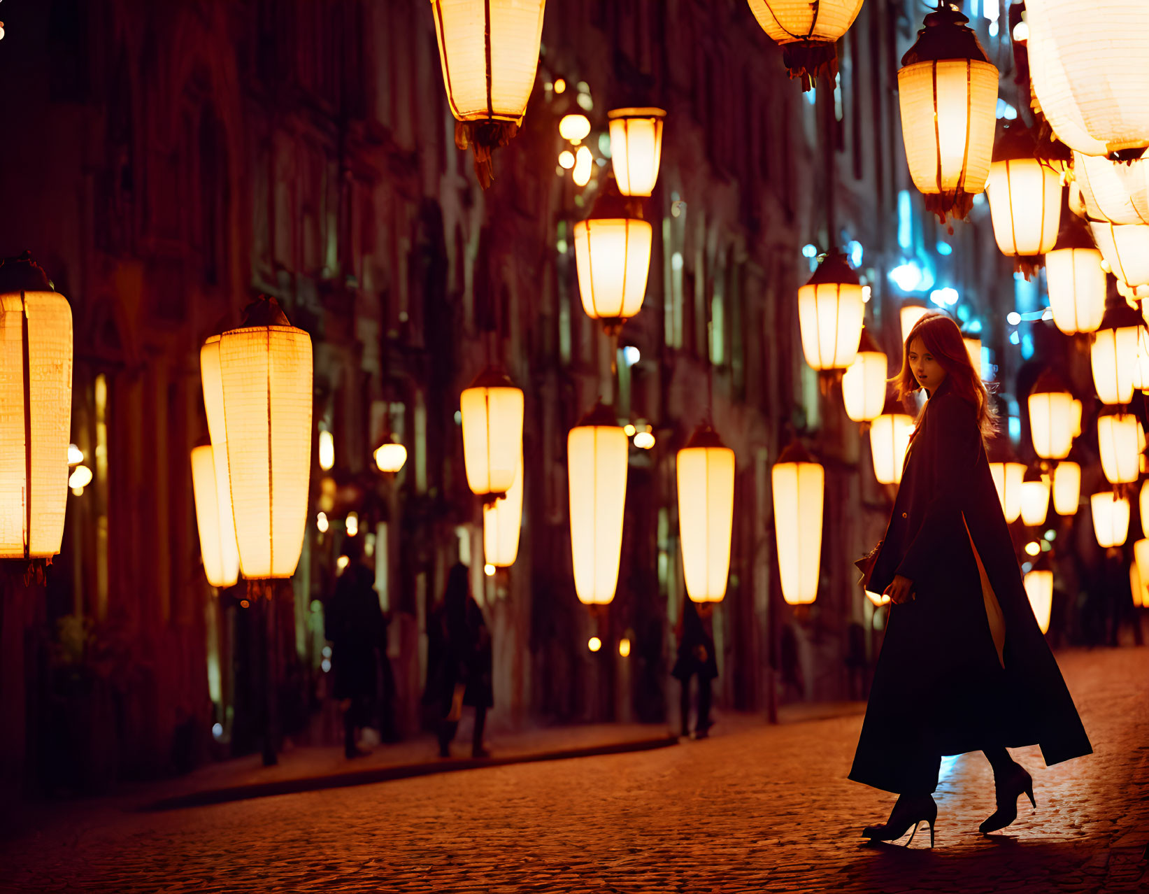 Woman in coat walking on cobblestone street at night under warm lantern light