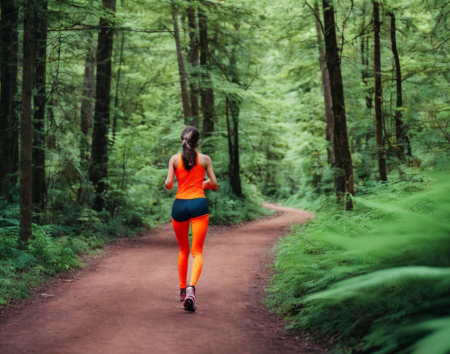 Woman jogging in bright orange and blue sportswear on forest dirt path