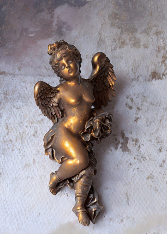 Bronze cherubic angel sculpture with wings and floral garland on textured wall