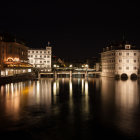 Night waterfront scene with illuminated houses and boats reflecting on calm water