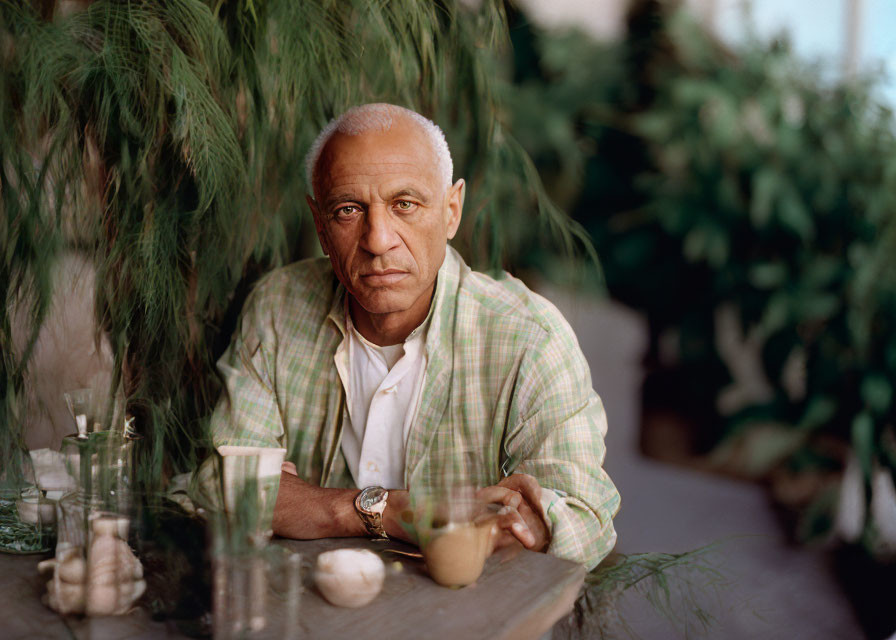 Elderly man sitting at table with drink amid green plants