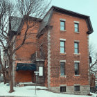 Abandoned three-story brick building with boarded windows and bare tree under clear skies