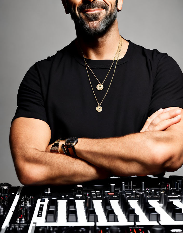 Bearded man in black shirt with gold necklaces by DJ mixer