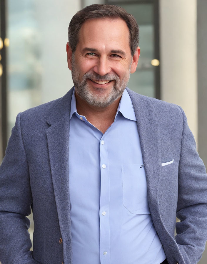 Smiling man in blazer and blue shirt by glass building