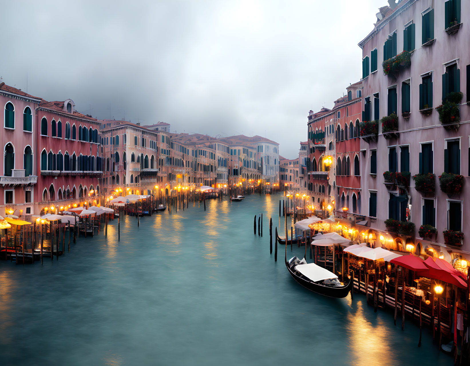 Misty Venetian canal at twilight with historic buildings and illuminated restaurants