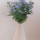 Transparent glass vase with blue flowers, green leaves, and scattered petals