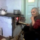 Elderly woman stoking fire in wood-burning stove with steam and autumn leaves