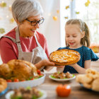 Elderly woman and young girl with freshly baked pie and fruits on table