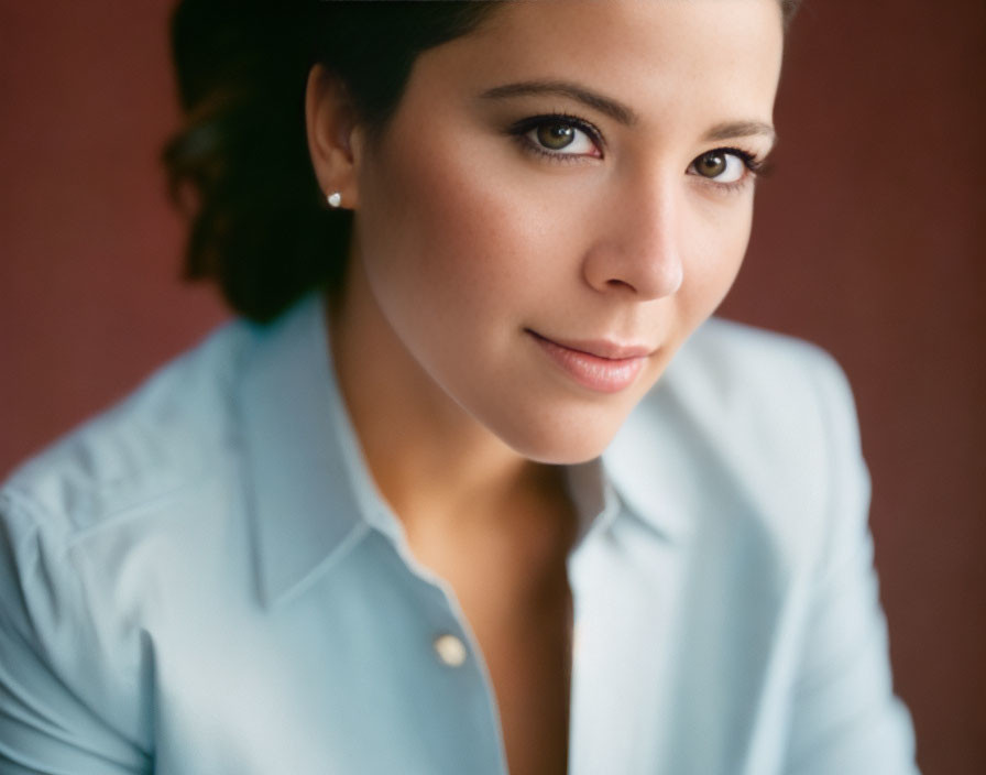 Portrait of woman with light brown hair, earrings, blue shirt, smiling warmly.