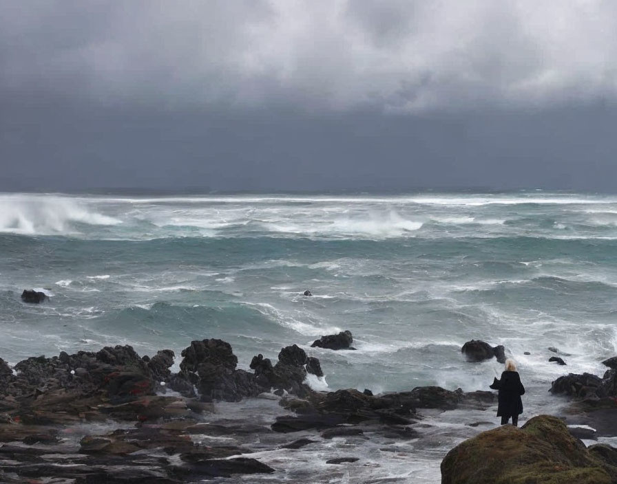 Person Standing on Rocky Shore Watching Turbulent Ocean Waves