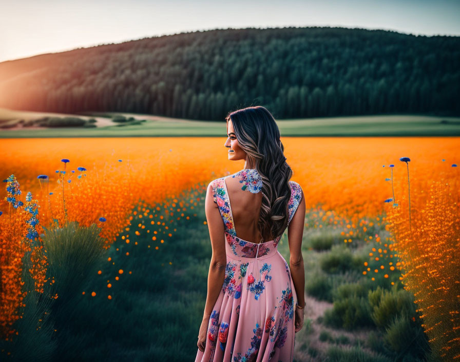 Woman in floral dress in vibrant orange flower field with green forest and dusky sky