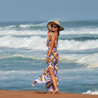 Woman in flowing dress and wide-brimmed hat by the sea under sunlight