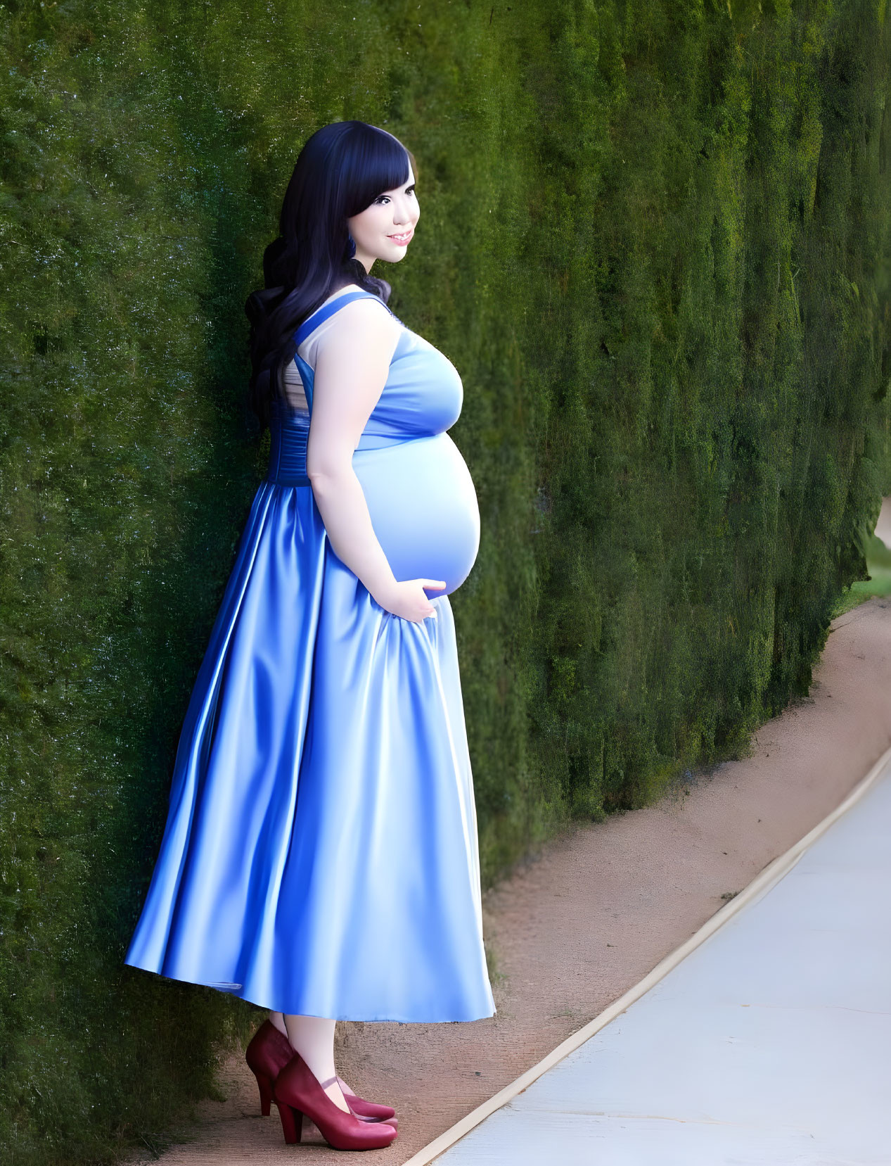 Pregnant woman in blue dress smiling beside green hedge