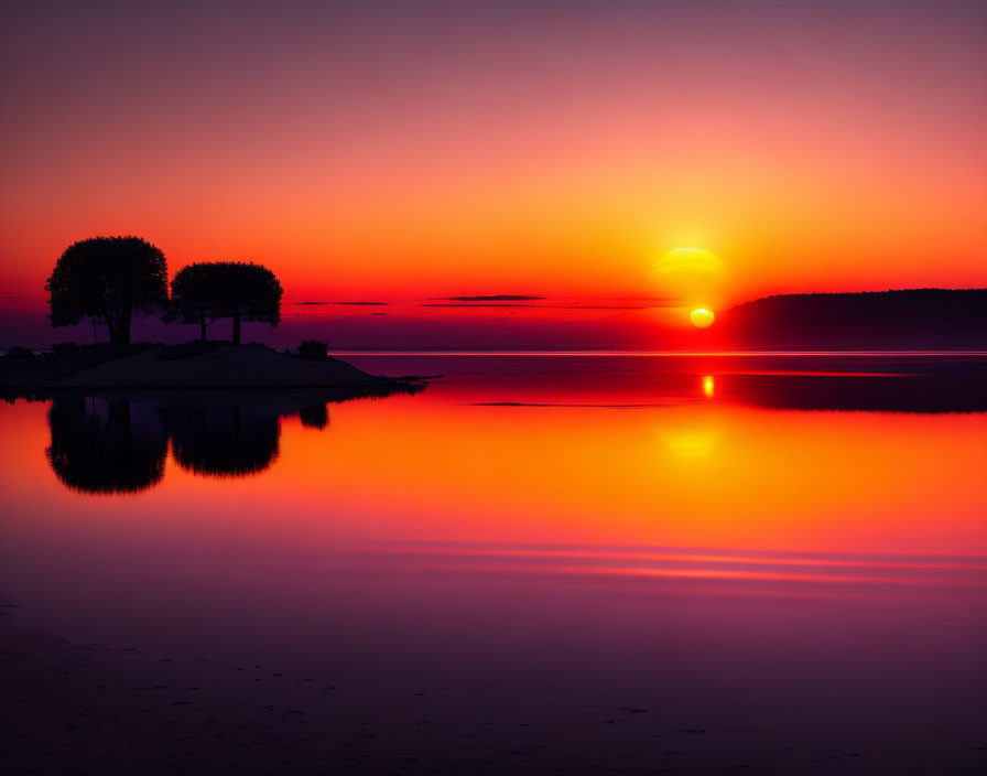 Scenic sunset with orange sun over still lake and tree silhouettes