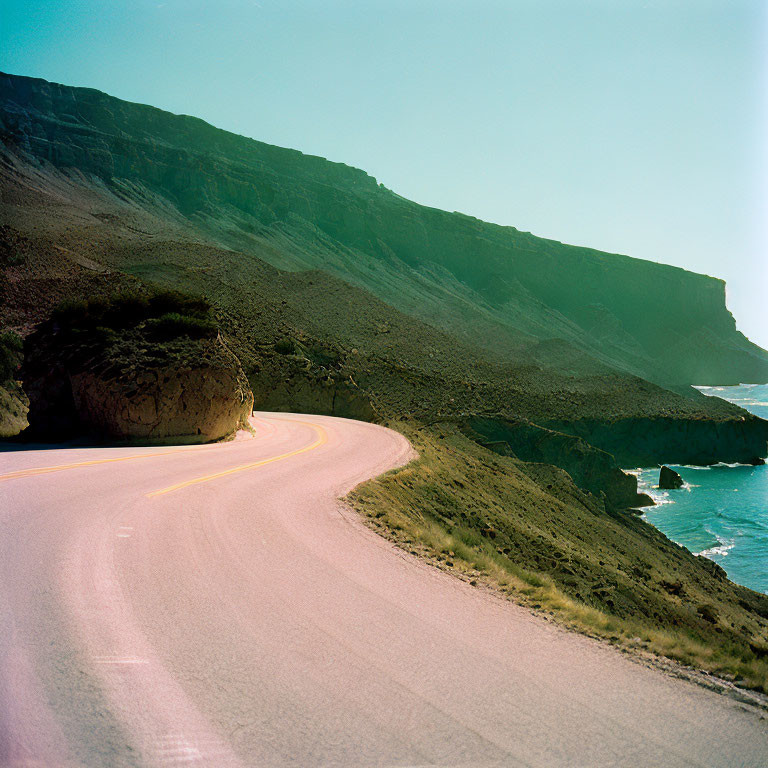 Scenic coastal landscape with curving road, steep cliffs, blue sea, and clear skies