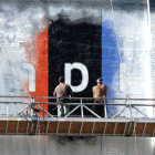 Weathered mural with abstract flag design and bold 'D' letter partially obscured by railing and machinery