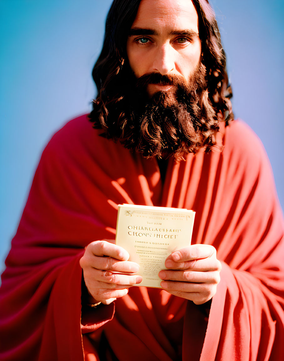 Bearded man in red robe holding Cyrillic text book on blue background