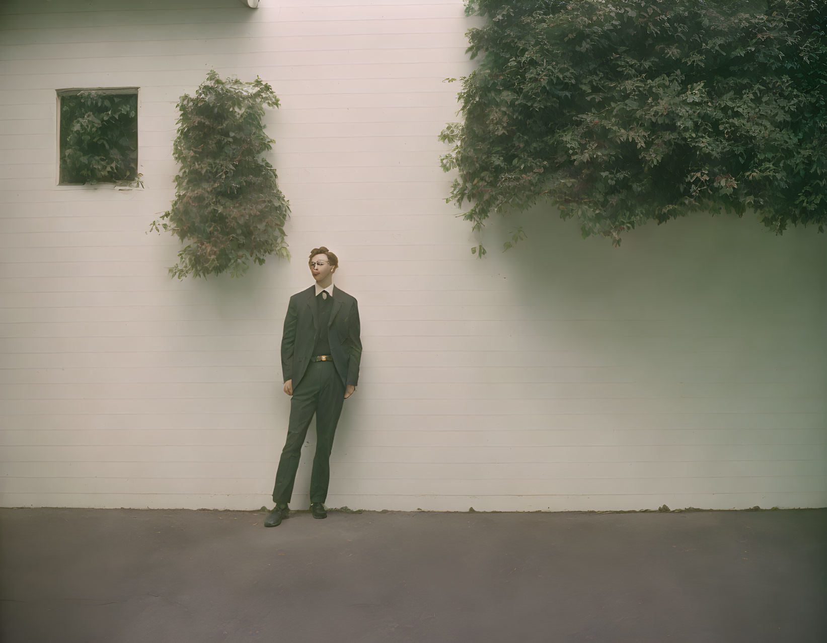 Businessman in suit and glasses by ivy-covered wall with window