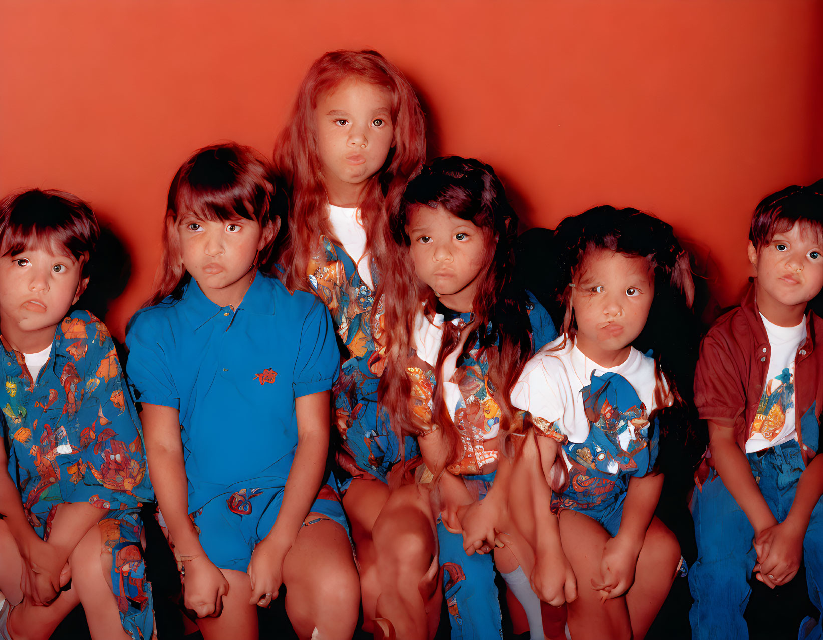 Five Children Sitting in Blue Outfits Against Red Background