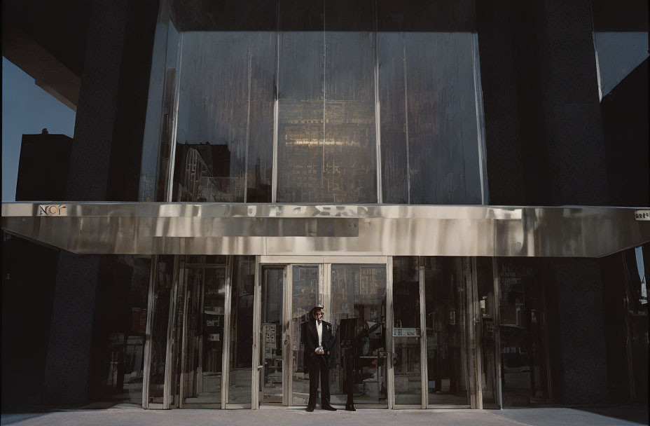 Businessman in suit at modern building entrance with metal awning.